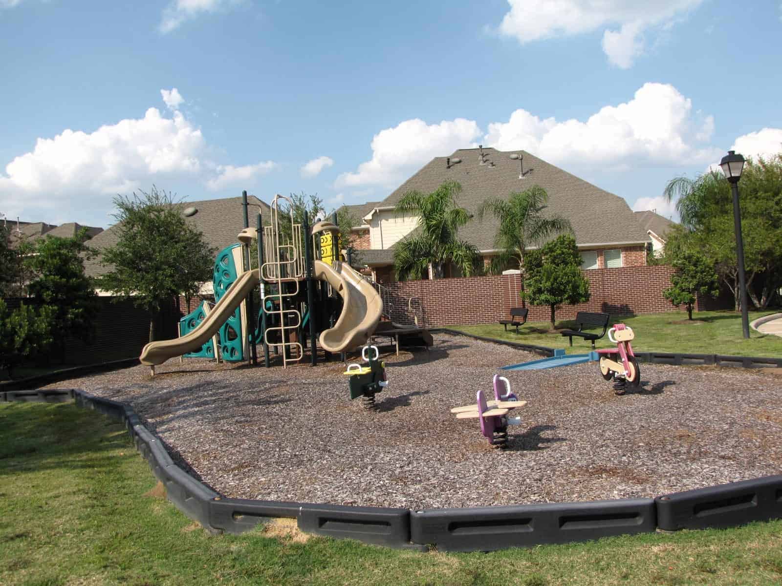 A Copper Lakes neighborhood playground with slides and climbing structures, benches, and shade trees in Houston, TX 77095