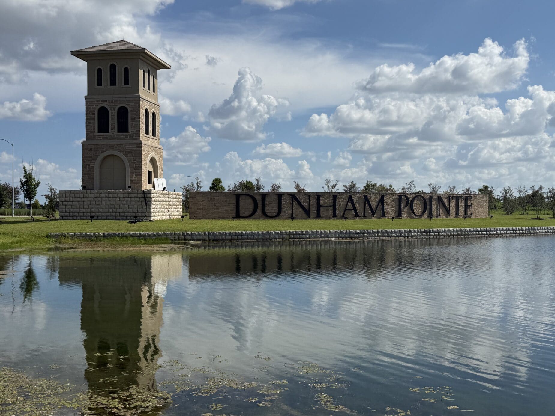The Dunham Pointe stone entry wall and tower beside the community pond — Cypress, TX 77433