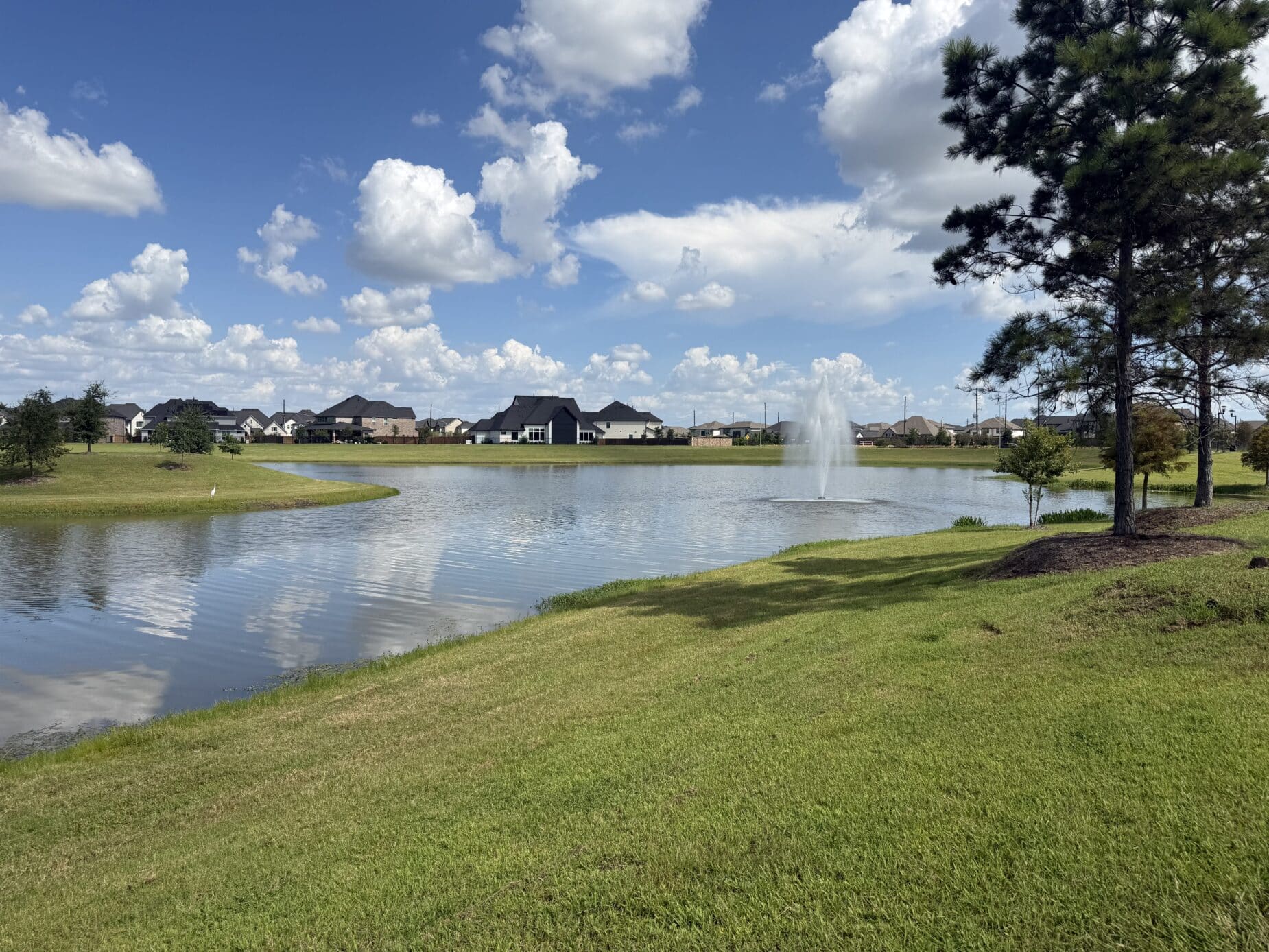 A Dunham Pointe lake with a fountain, shade trees, and homes on the far bank — Cypress, TX 77433