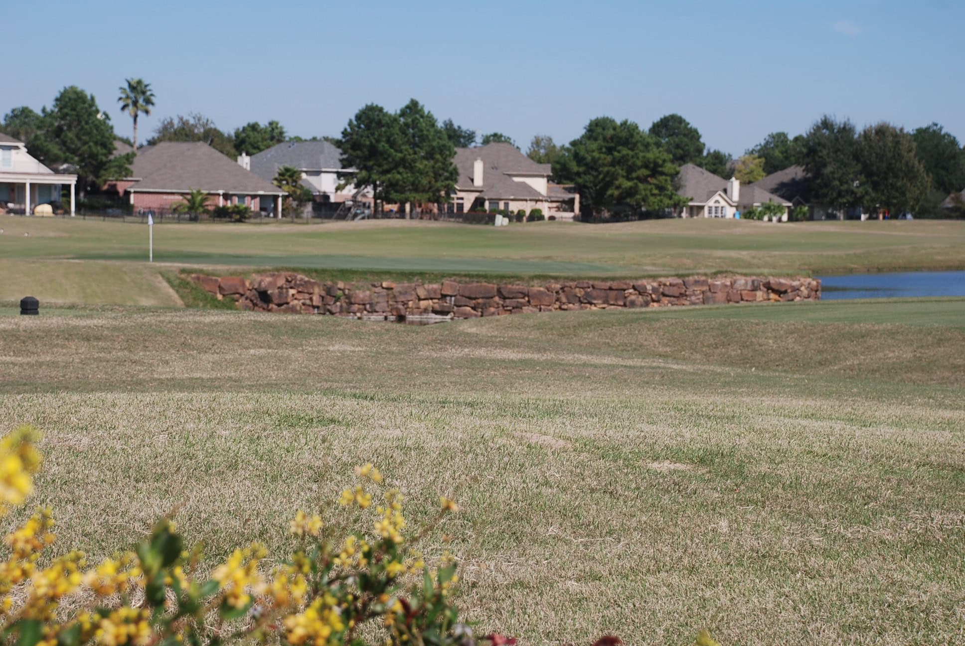 Fairway, stone wall and lake at Houston National Golf Club with Stone Gate homes beyond