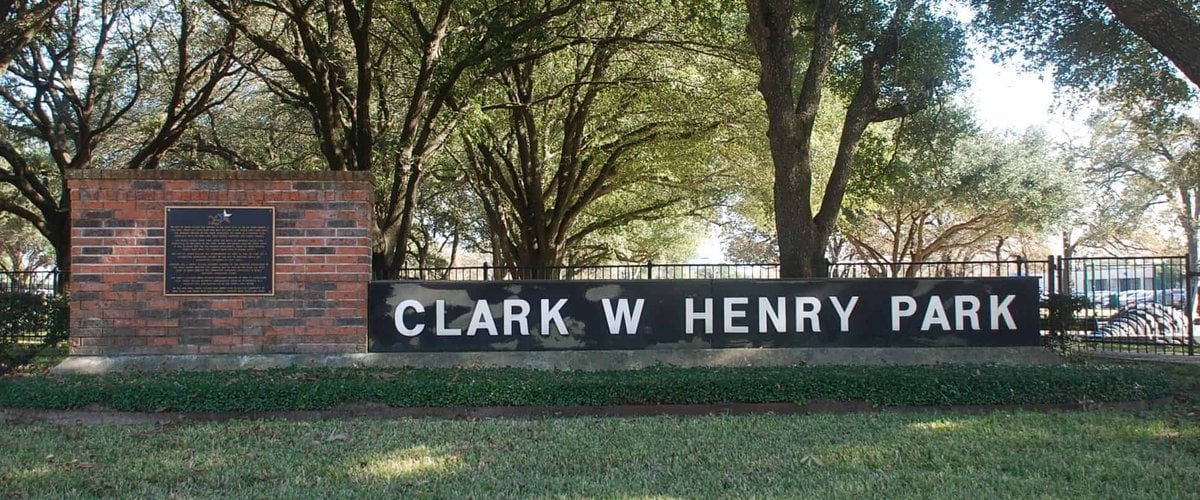 Clark W. Henry Park entrance sign and brick pillar with the city history plaque, under live oaks in Jersey Village, TX