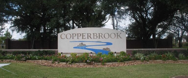 Copperbrook entrance sign with a brick wall, flower beds and mature oaks, Houston TX 77095
