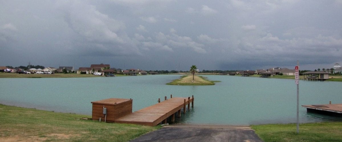 Boat ramp and wooden dock on a turquoise lake with a palm-topped island and homes beyond, Lakes of Katy, Katy TX 77493