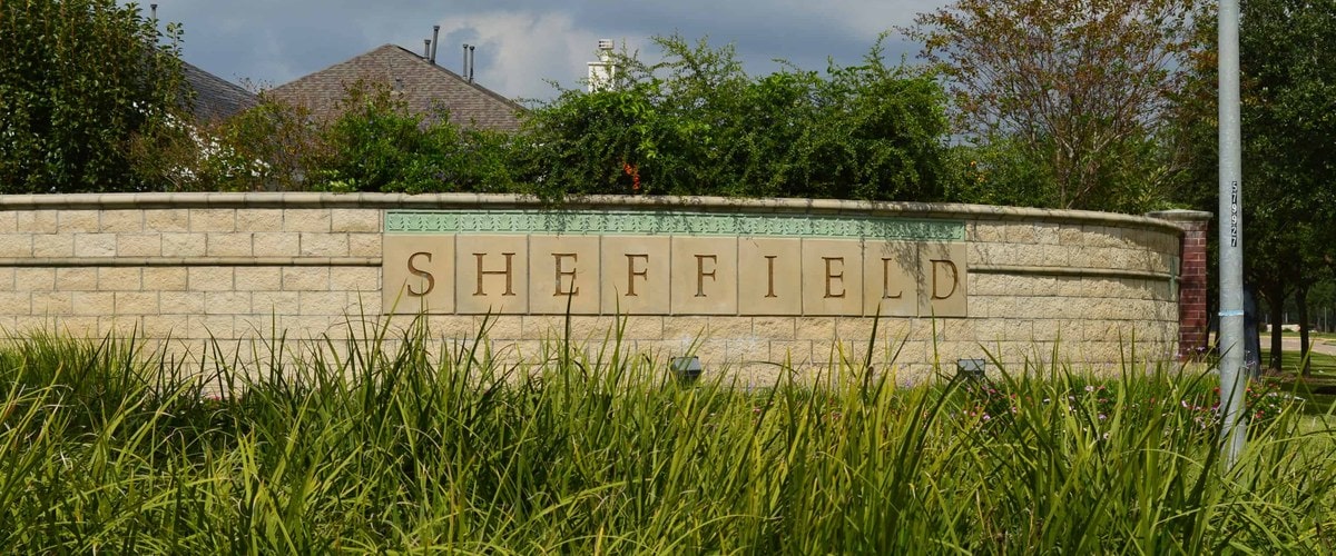 Stone Sheffield entrance monument with ornamental grasses and mature trees, Houston TX 77095