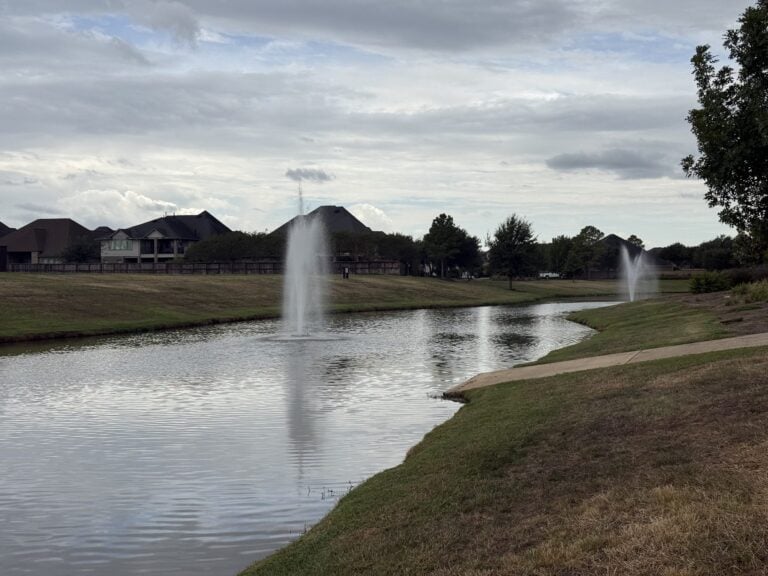 Lake with a fountain and homes along the far bank in Cane Island, Katy TX 77493