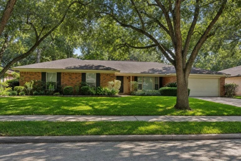 A single-story 1960s brick ranch house on a tree-lined Houston street, the kind of slab-on-grade home that often has cast iron pipes under the slab