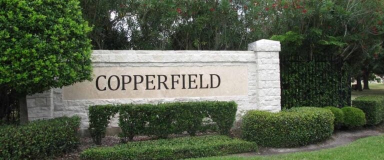 COPPERFIELD stone entrance monument framed by clipped hedges and flowering shrubs, Houston TX 77095