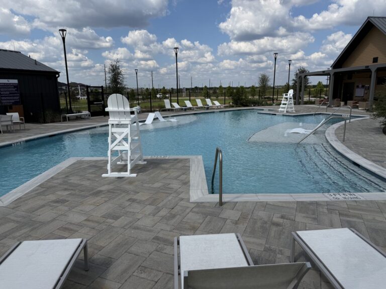 Everly community pool with a lifeguard stand, sun shelf, and lounge chairs on a paver deck, Hockley TX 77447