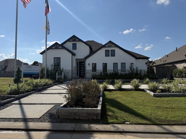 One-story DRB Homes model with a white brick front, a wide walk and flagpoles, Oakwood Estates, Waller TX 77484