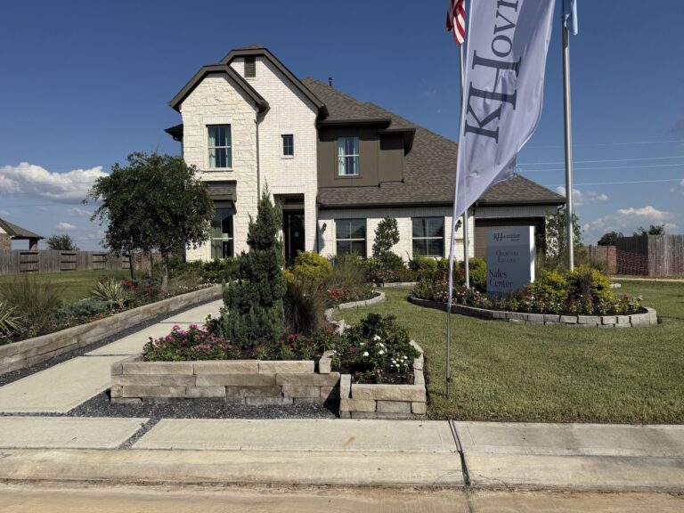 Two-story K. Hovnanian model home with a light stone front, landscaped beds and a K. Hovnanian flag, Oakwood Estates, Waller TX 77484