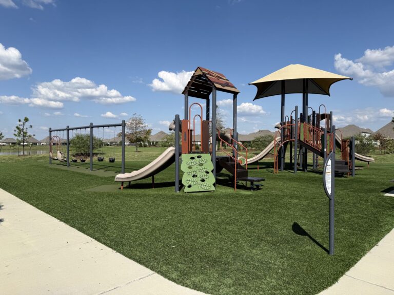 Oakwood Estates playground with slides, swings and a shade canopy on a green lawn, Waller TX 77484