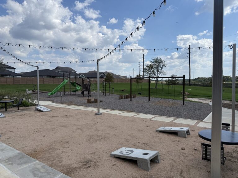 Lawn-game area with cornhole boards and string lights beside the playground in Redbud, Hockley TX 77447