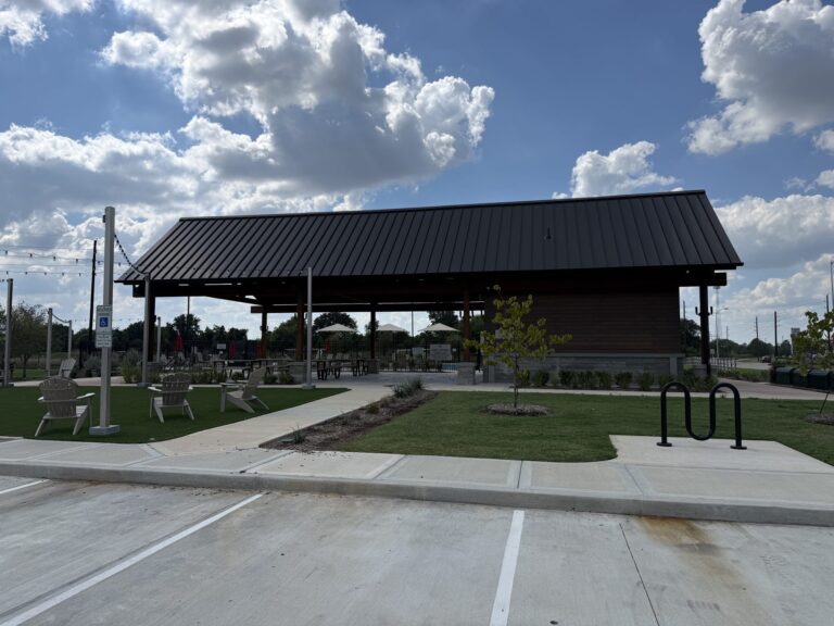 Covered pavilion with a metal roof, lawn, and Adirondack chairs at the Redbud amenity center, Hockley TX 77447