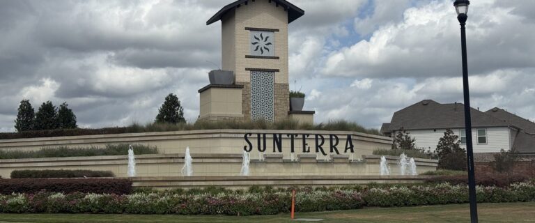 Sunterra entry monument with fountains and a stone tower under a cloudy sky, Katy TX 77493