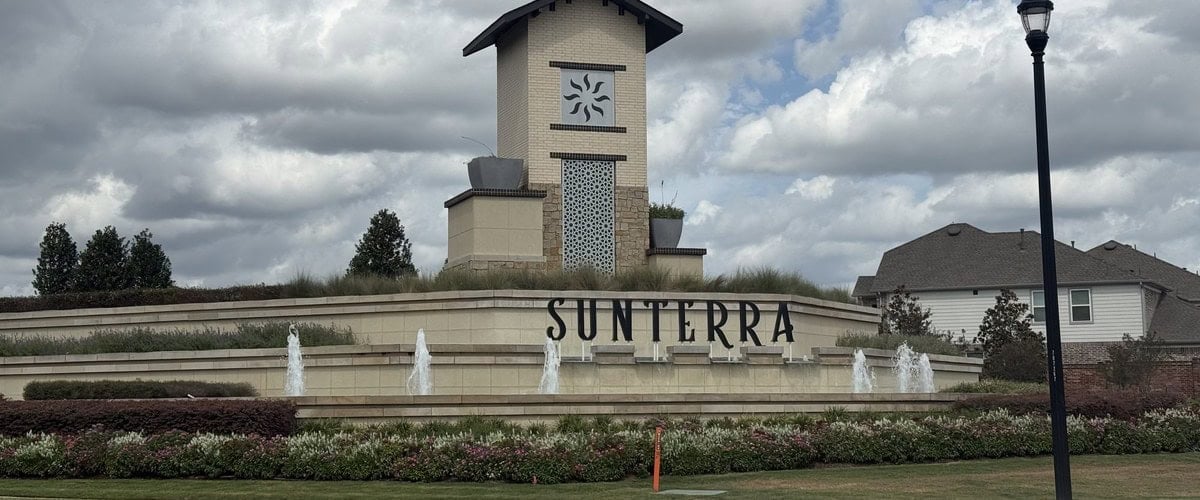 Sunterra entry monument with fountains and a stone tower under a cloudy sky, Katy TX 77493