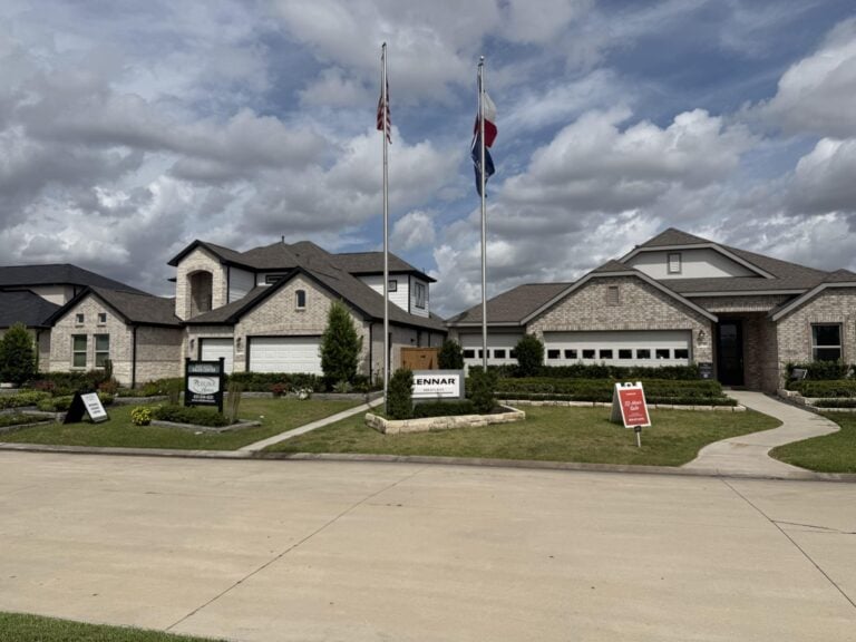 Row of builder model homes with flags along a street in Sunterra, Katy TX 77493