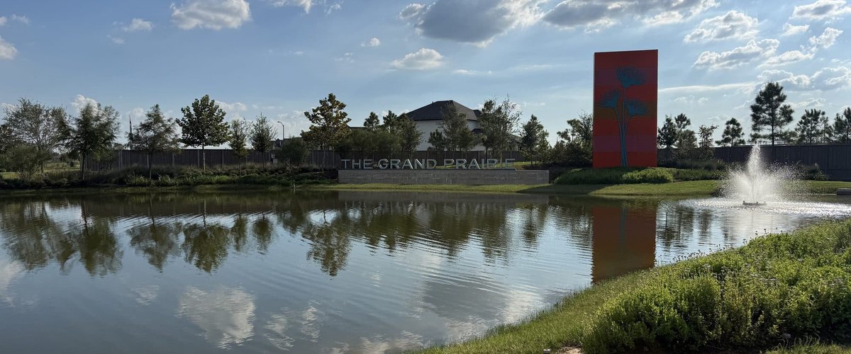 THE GRAND PRAIRIE entry sign and a red monument tower beside a pond with a fountain, Hockley TX 77447