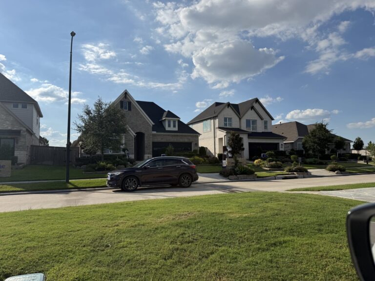 Brick and stone David Weekley Homes model with landscaped beds and a model-home sign, beside other builder models, Hockley TX 77447