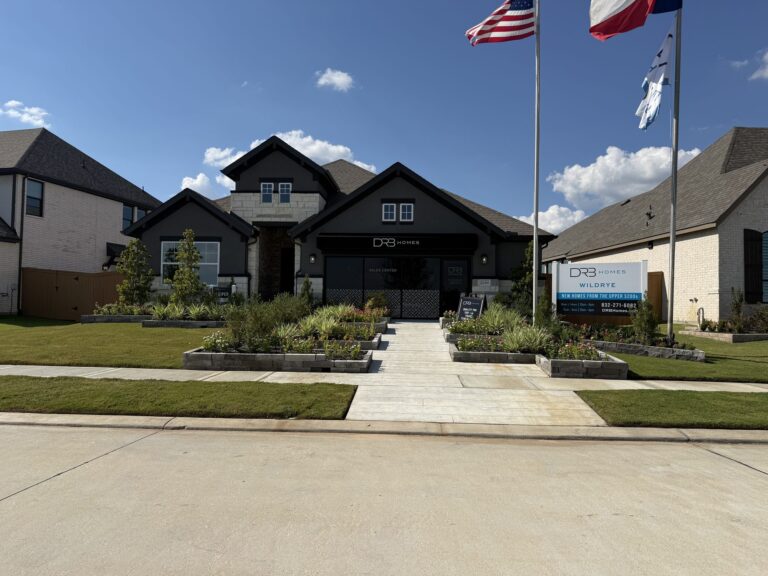 Dark-sided DRB Homes model with a landscaped front walk and flags, Wildrye, Waller TX 77484